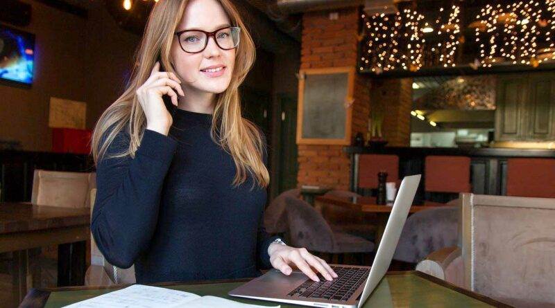 Eine Frau sitzt mit einem Laptop und einem Notebook an einem Tisch.