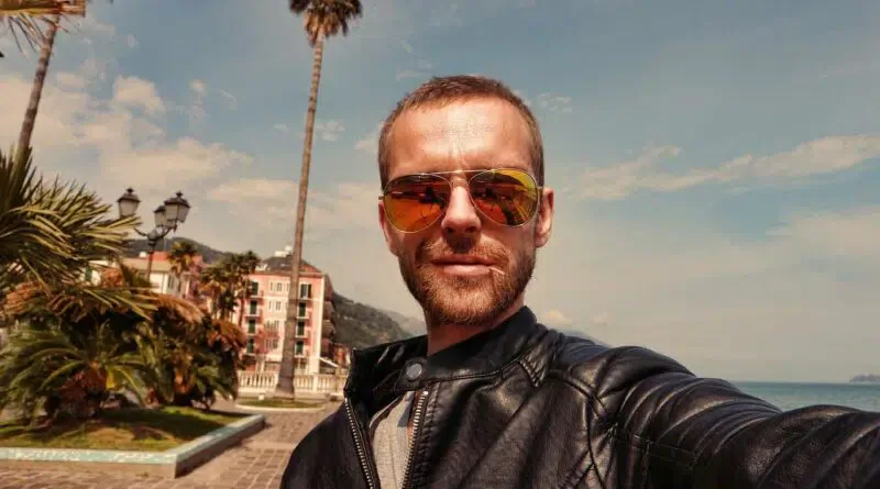 Ein Mann macht ein Selfie vor einer Palme.