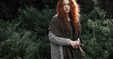 Eine Frau mit roten Haaren steht in einem Wald.