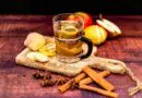 Eine Tasse Glühwein mit Zimtstangen und Äpfeln auf einem Holzbrett.
