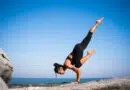 Eine Frau übt Yogaklassen, indem sie einen Handstand auf einem Felsen vor dem Meer macht.