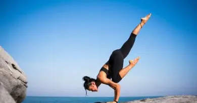 Eine Frau übt Yogaklassen, indem sie einen Handstand auf einem Felsen vor dem Meer macht.