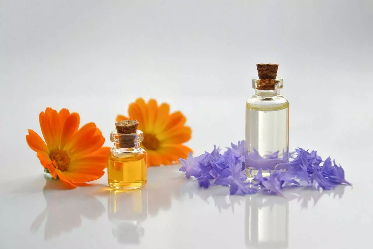 Eine Flasche ätherisches Öl und Blumen auf einer weißen Oberfläche.