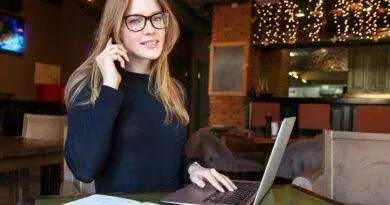 Eine Frau sitzt mit einem Laptop und einem Notebook an einem Tisch.