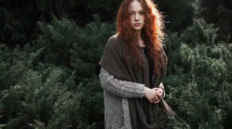 Eine Frau mit roten Haaren steht in einem Wald.