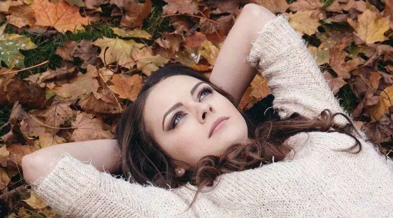 Eine Frau, die im Herbstmode mit den Herbstblättern verschmilzt.