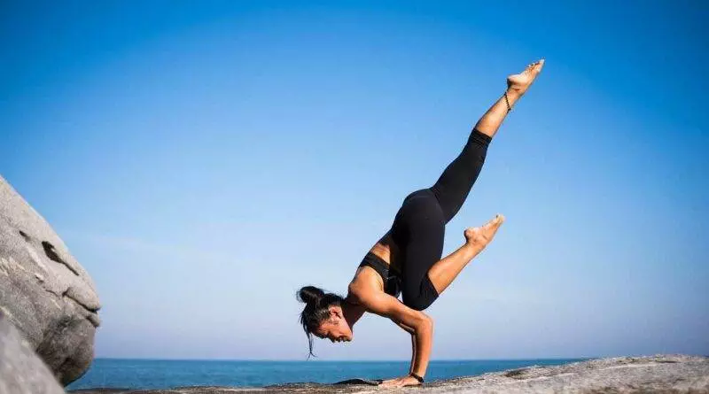 Eine Frau übt Yogaklassen, indem sie einen Handstand auf einem Felsen vor dem Meer macht.