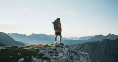 Ein Mann steht mit einem Rucksack auf einem Berggipfel.