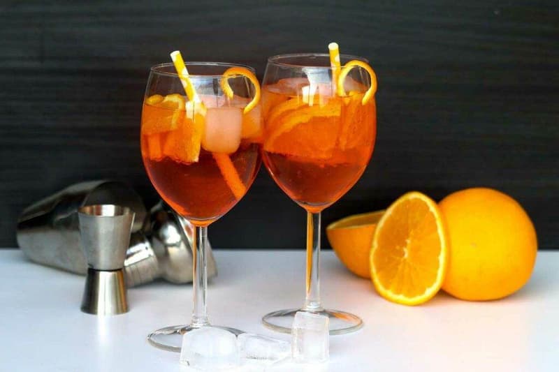 Zwei Gläser Cocktail mit Orangenscheiben und Eis.