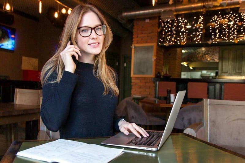 Eine Frau sitzt mit einem Laptop und einem Notebook an einem Tisch.