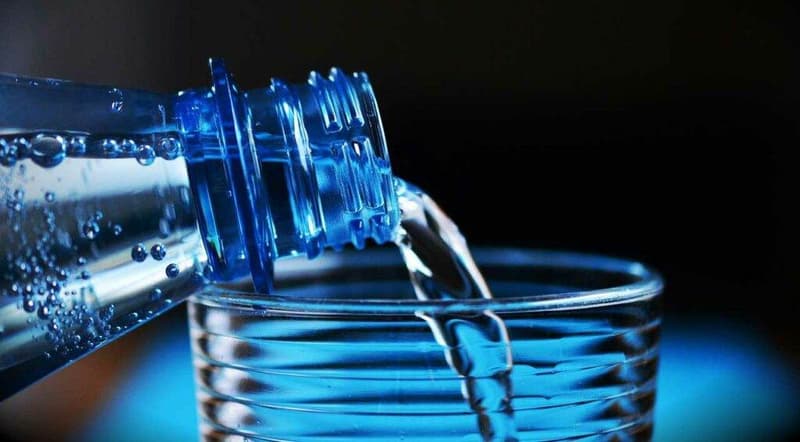 Eine Flasche Wasser wird in ein Glas gegossen.