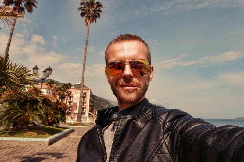 Ein Mann macht ein Selfie vor einer Palme.