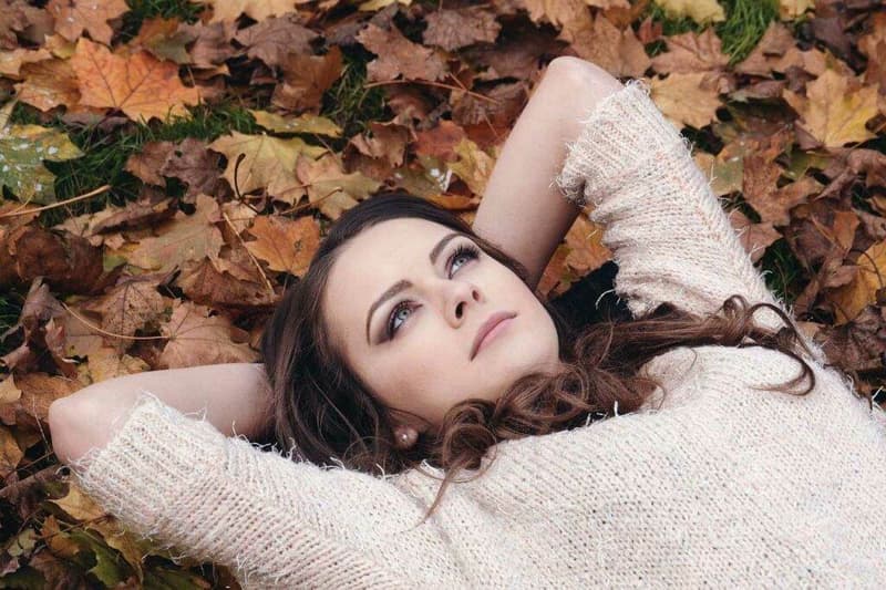 Eine Frau, die im Herbstmode mit den Herbstblättern verschmilzt.