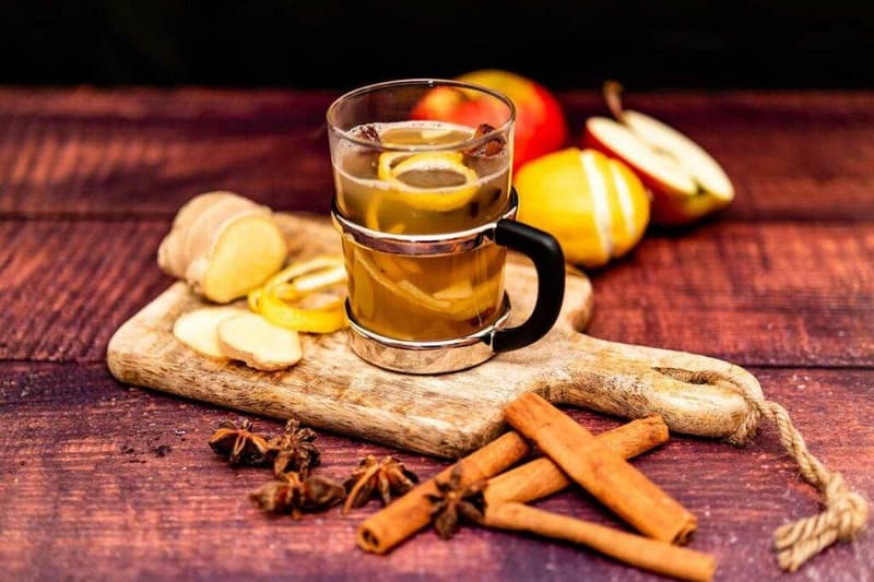 Eine Tasse Glühwein mit Zimtstangen und Äpfeln auf einem Holzbrett.