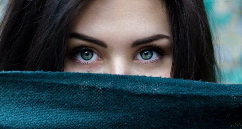 Eine Frau mit grünen Augen schaut aus einem Schal hervor.