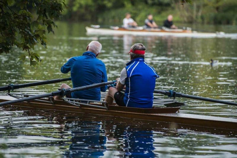 Zwei Männer rudern in einem Ruderboot auf einem See.